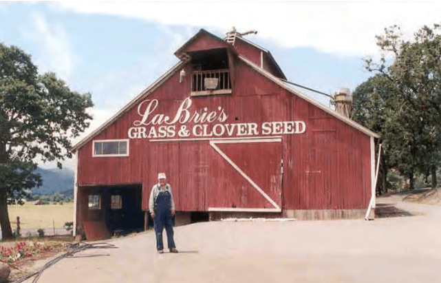 Red barn with La Brie's grass and clover seed written on it and farmer standing in front