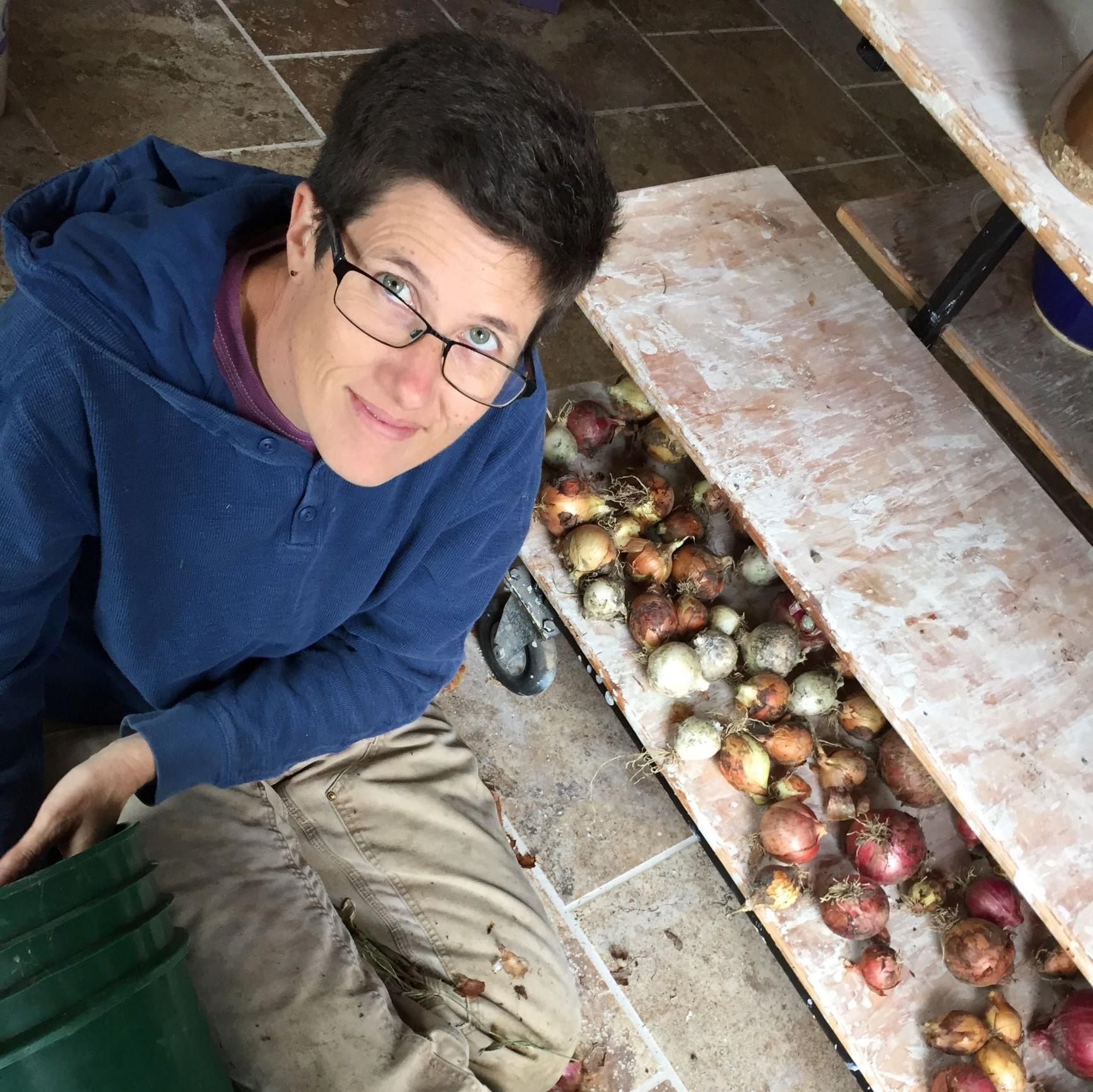 Smiling woman with glasses posing with onion harvest.