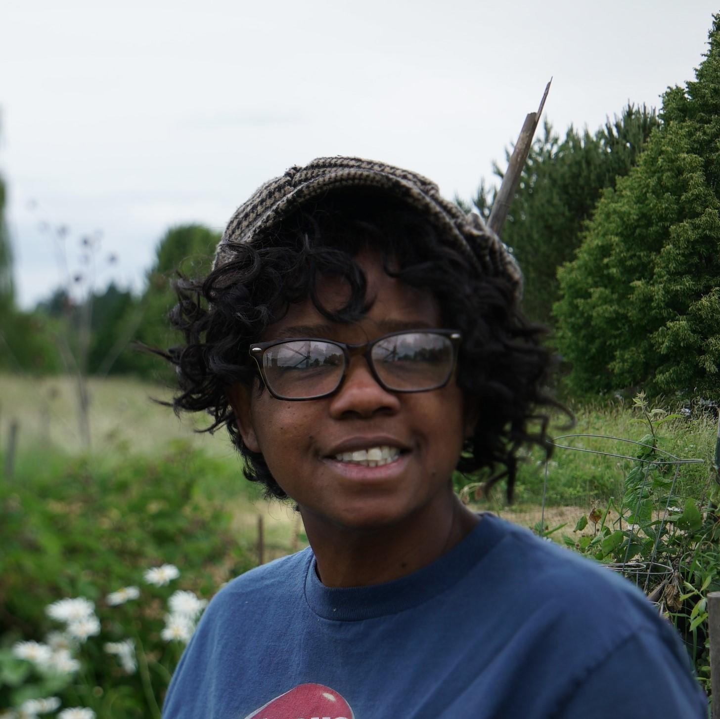 Smiling woman with glasses and hat in a garden.