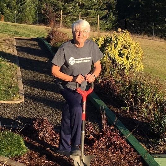 Smiling woman with shovel in a rose garden.