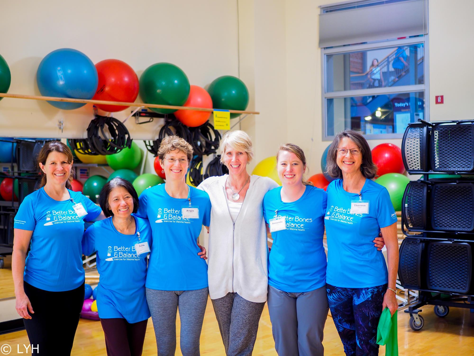 6 women standing together, smiling in a gym