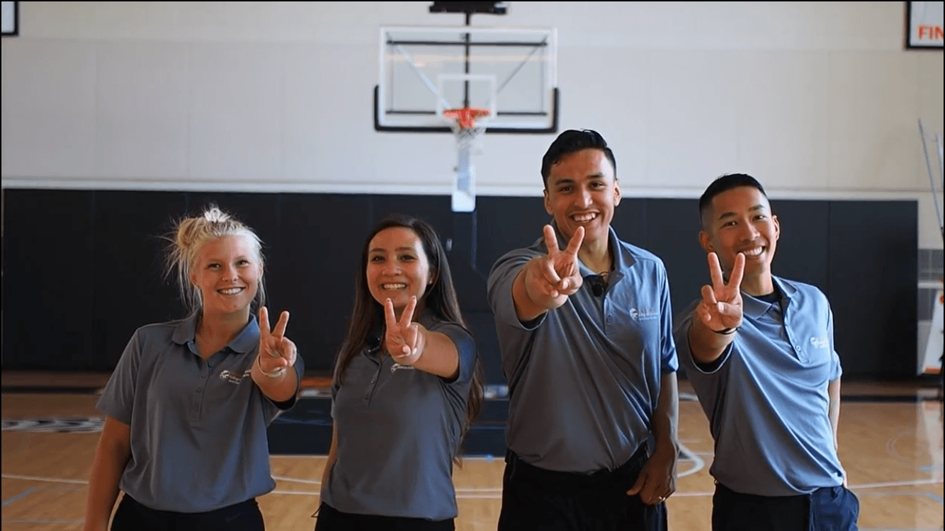 Four youth holding up two fingers on a basketball court