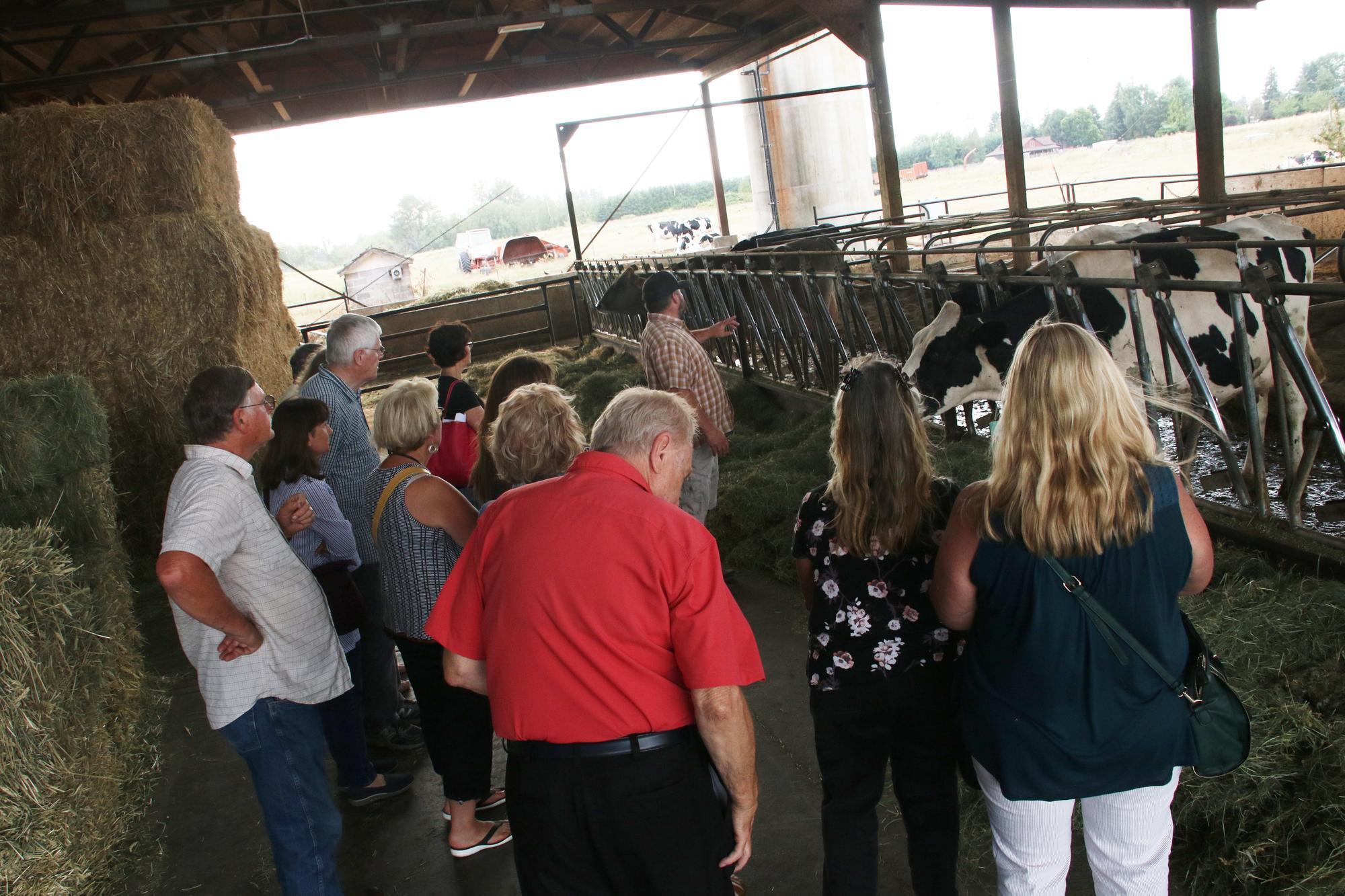 A group of people stand in a barn on a dairy farm as a tour guide talks about the facilities.