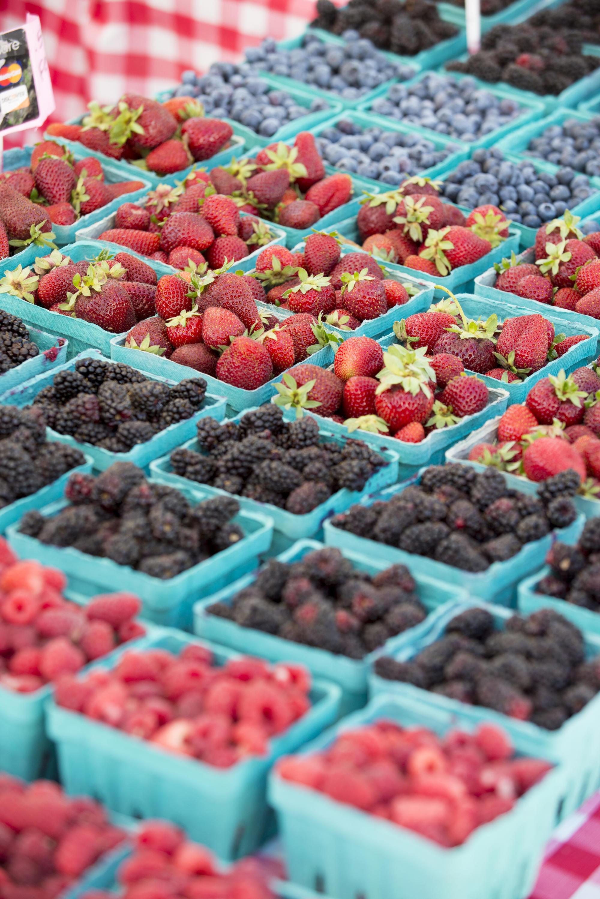 Boxes of berries -- raspberries, blackberries, strawberries and blueberries -- sit on a table at a farmers market.