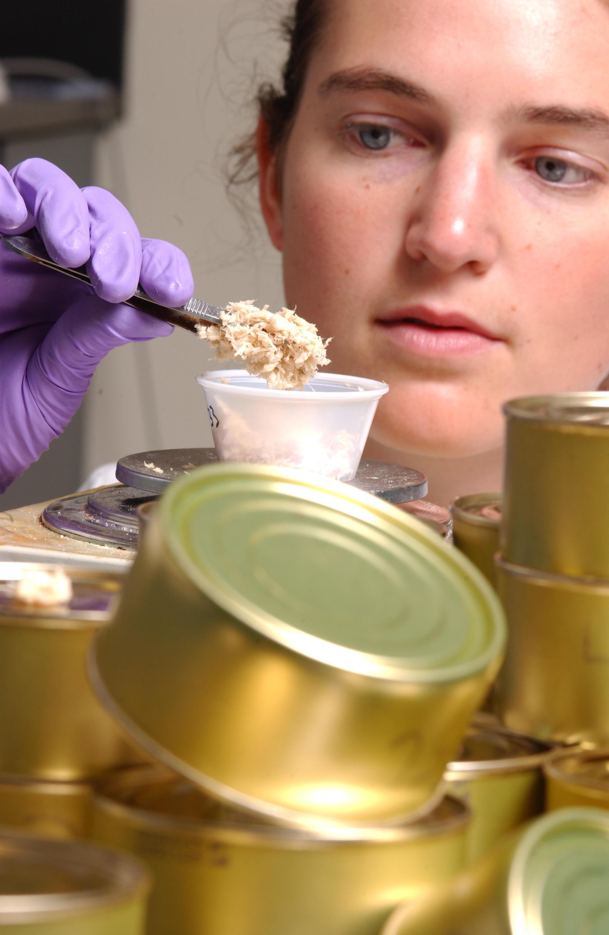 A woman inspects a sample of canned tuna.