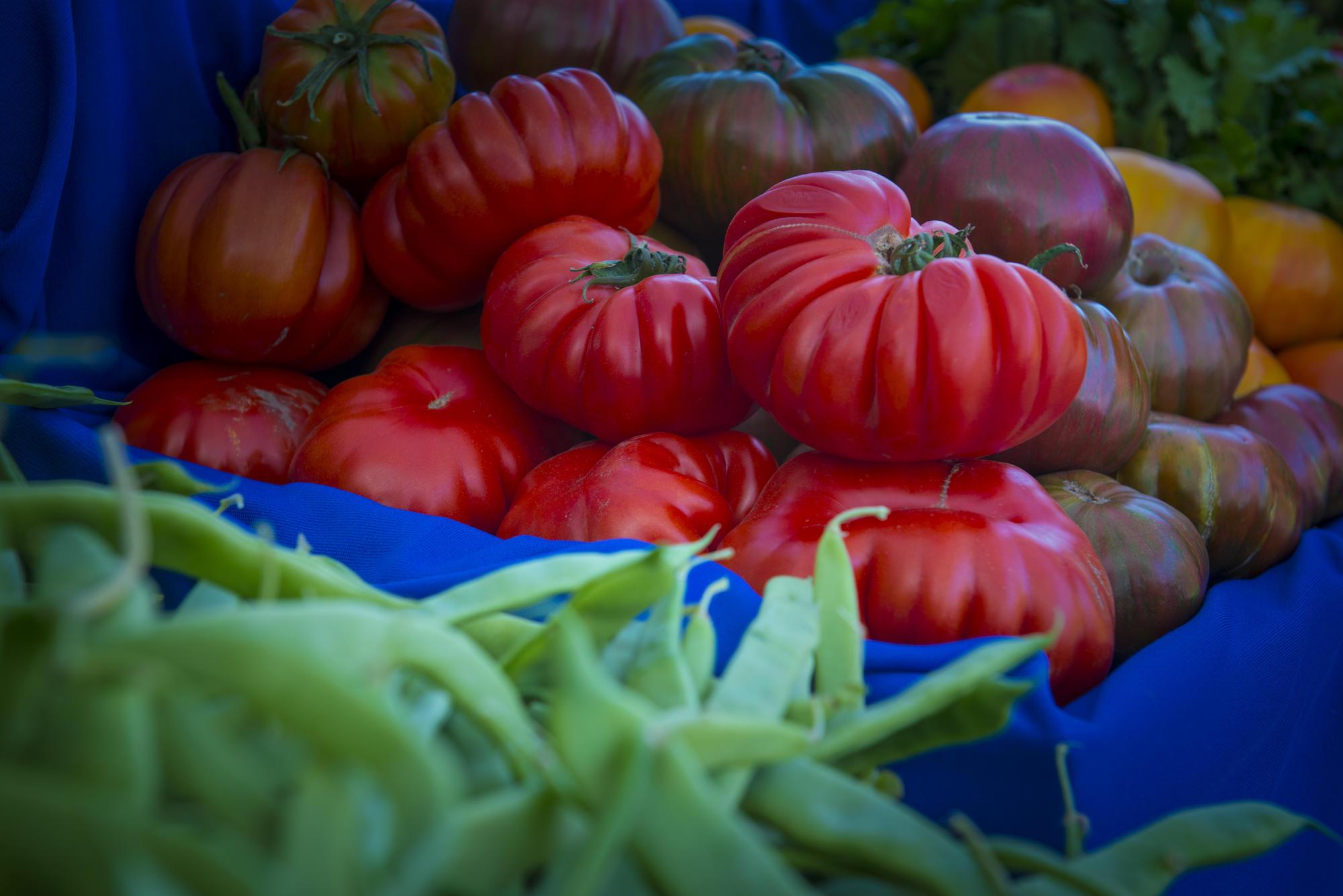 Ripe tomatoes are displayed on a table with other produce.