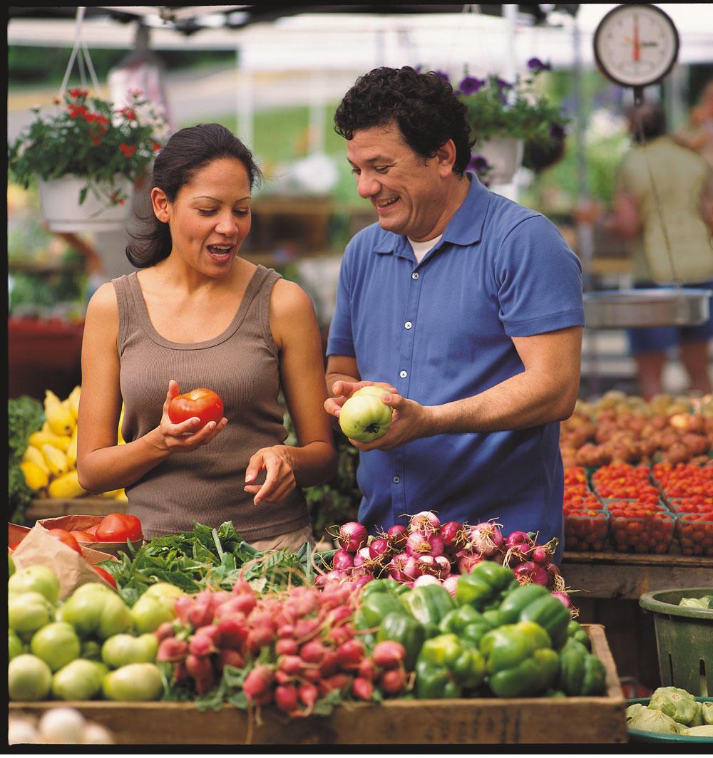 A man and woman look at produce at a farmers market.