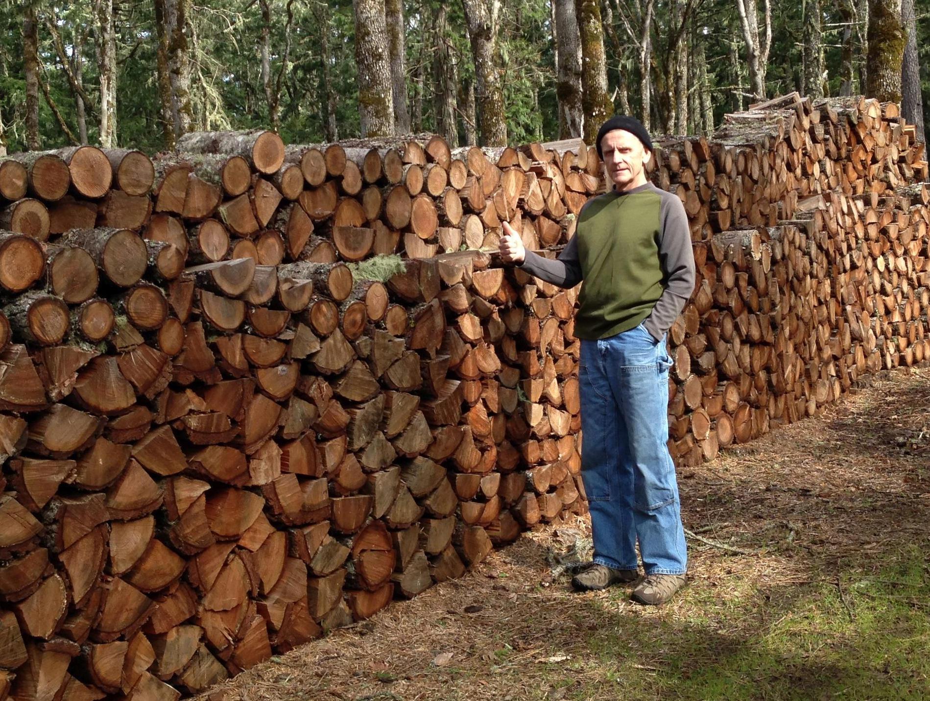 man standing next to long pile of firewood