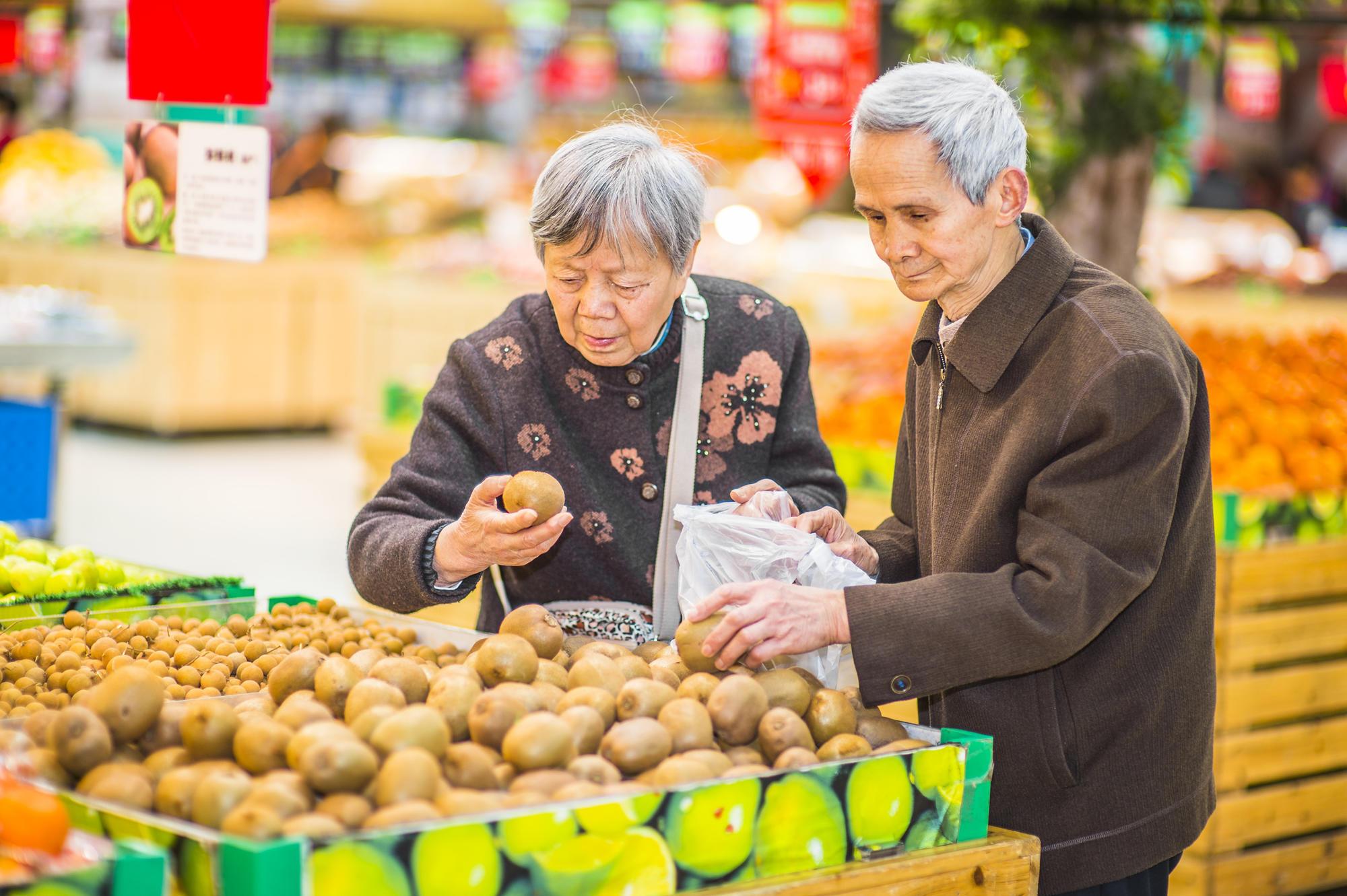 Older couple handle kiwi fruit in a market