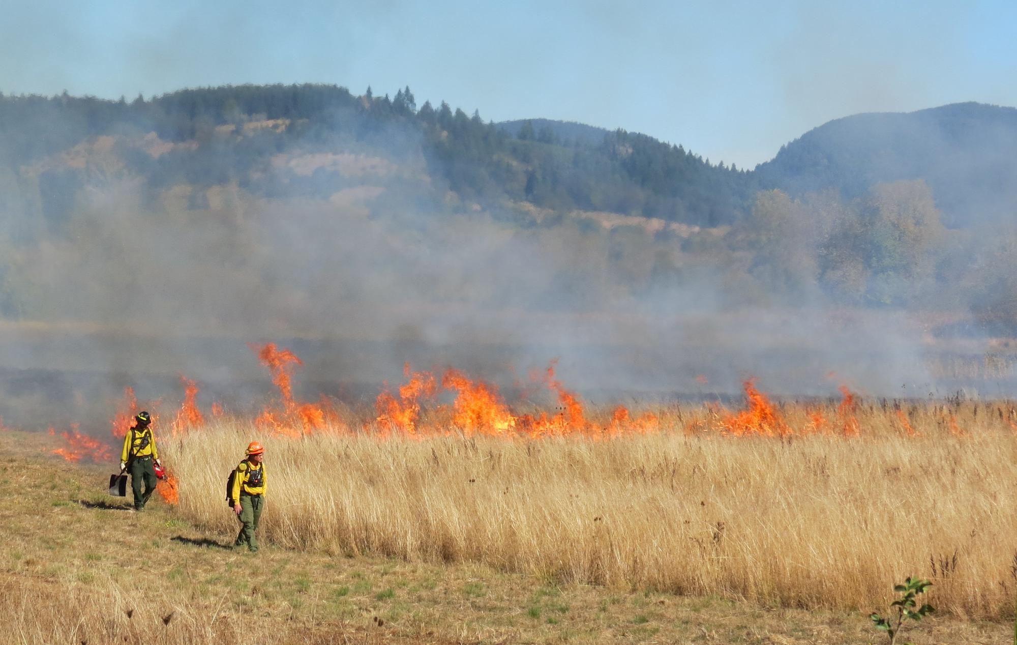 Two people move away from flames at the base of a hill