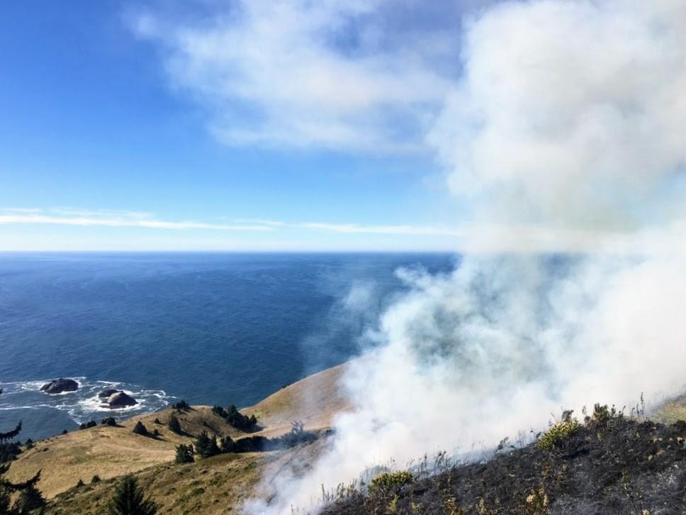 smoke rises over oceanside bluff on sunny day