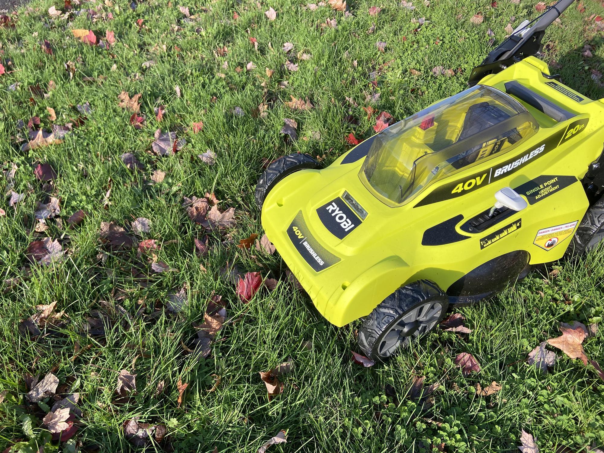 bright green electric lawn mower on lawn with fallen leaves