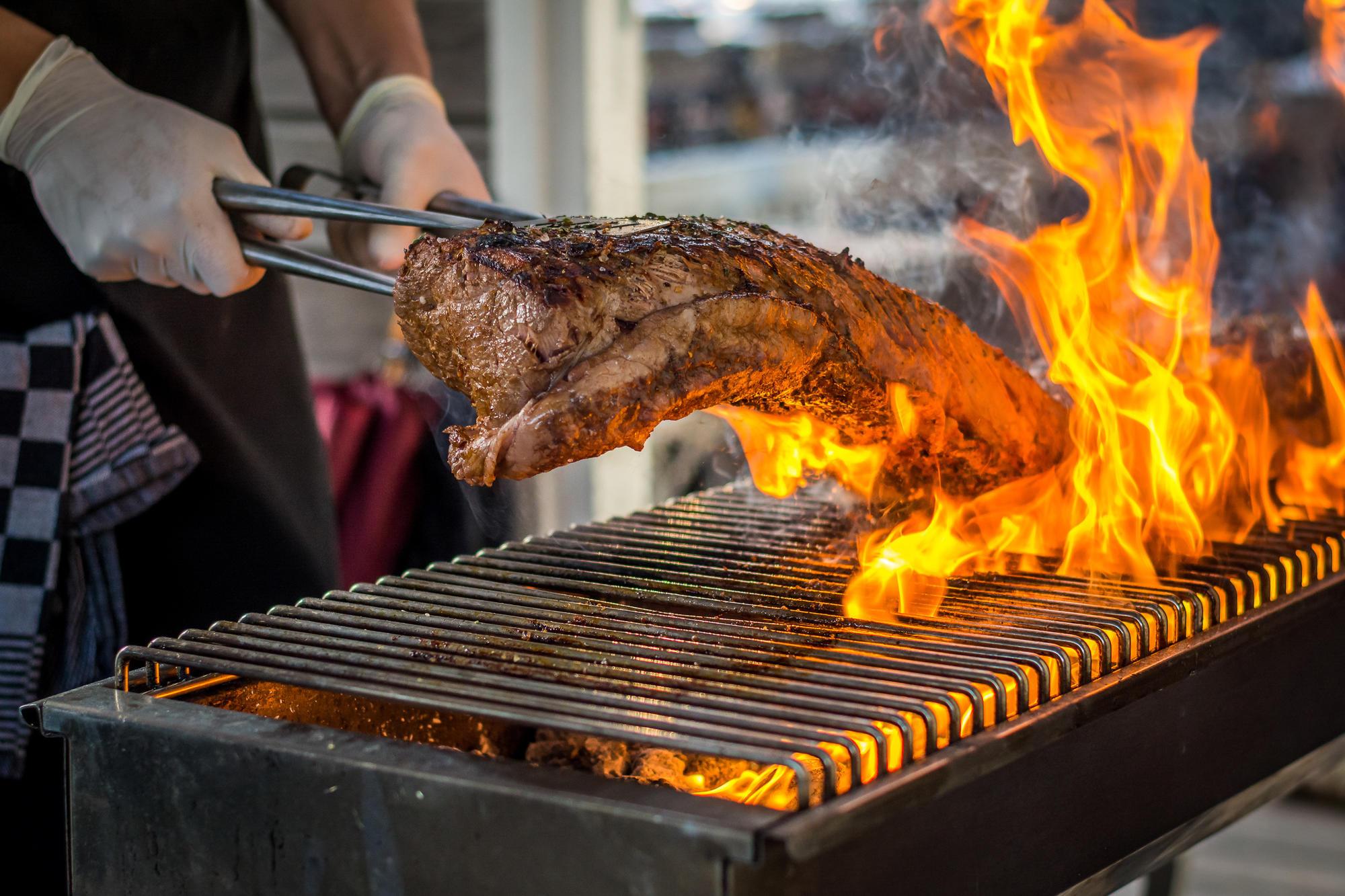 A person grills meat over an open flame.