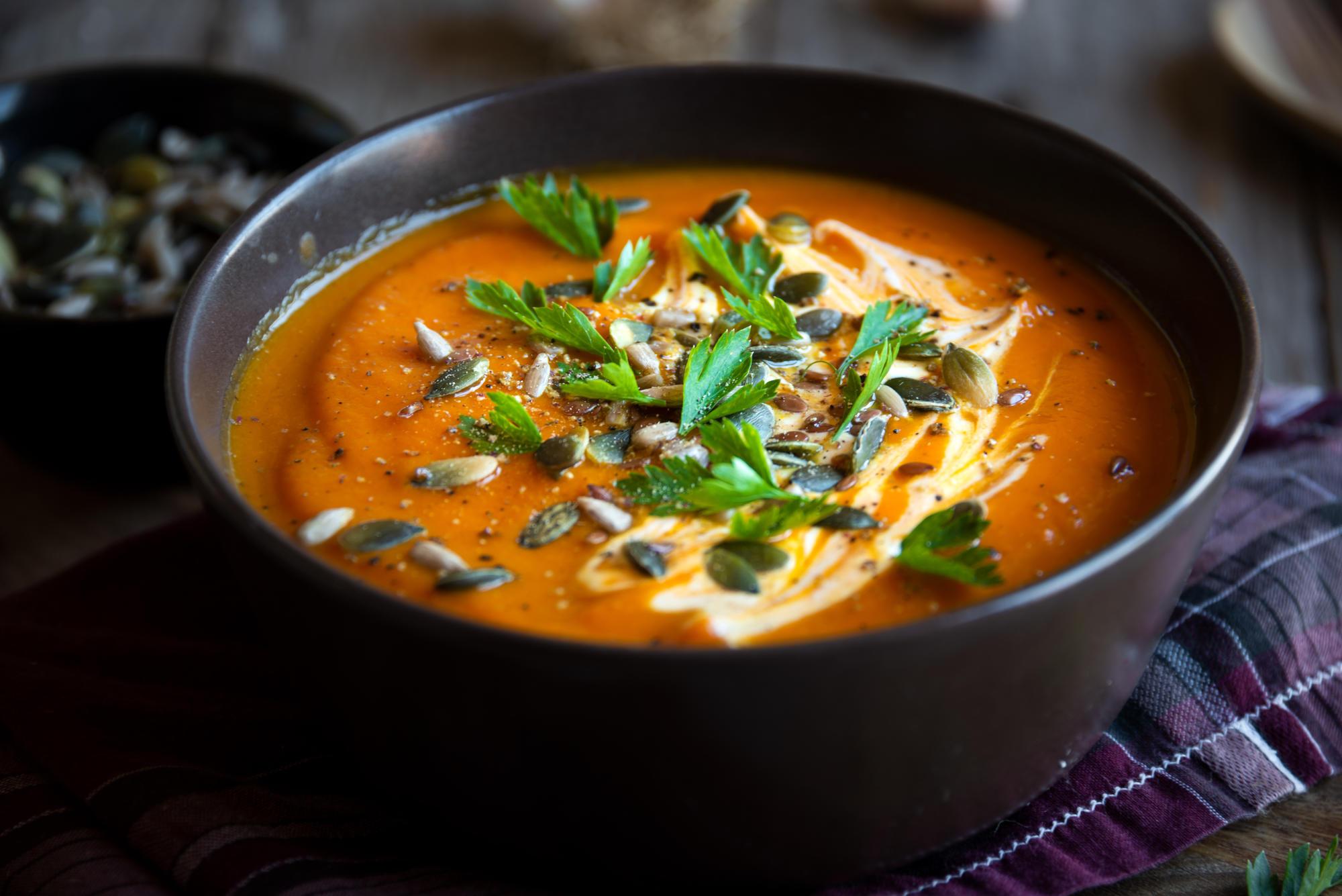 A bowl of pumpkin soup topped with pumpkin seeds, sour cream, and herbs.