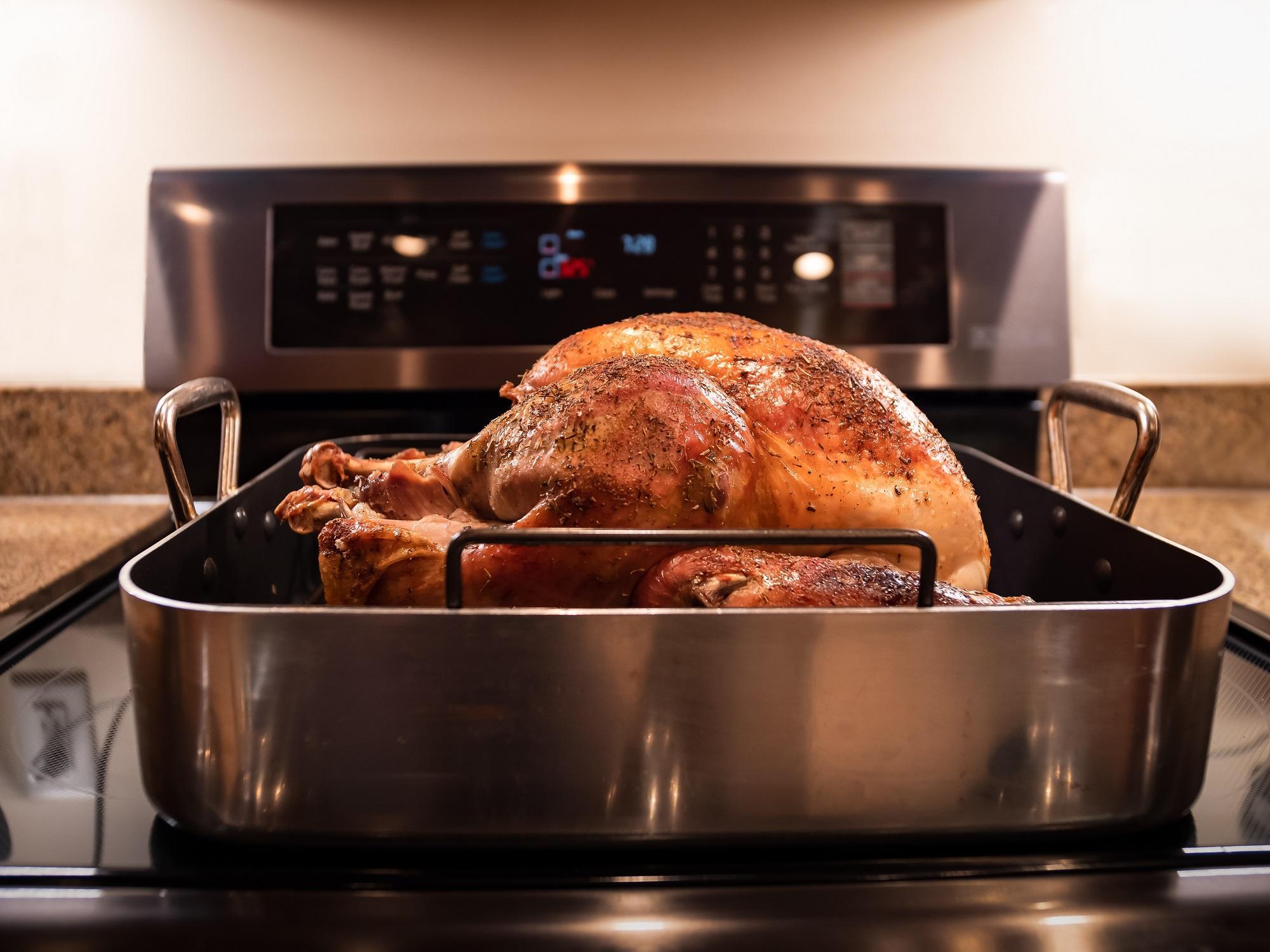 A cooked and seasoned turkey cooling in a roasting pan on a stovetop.