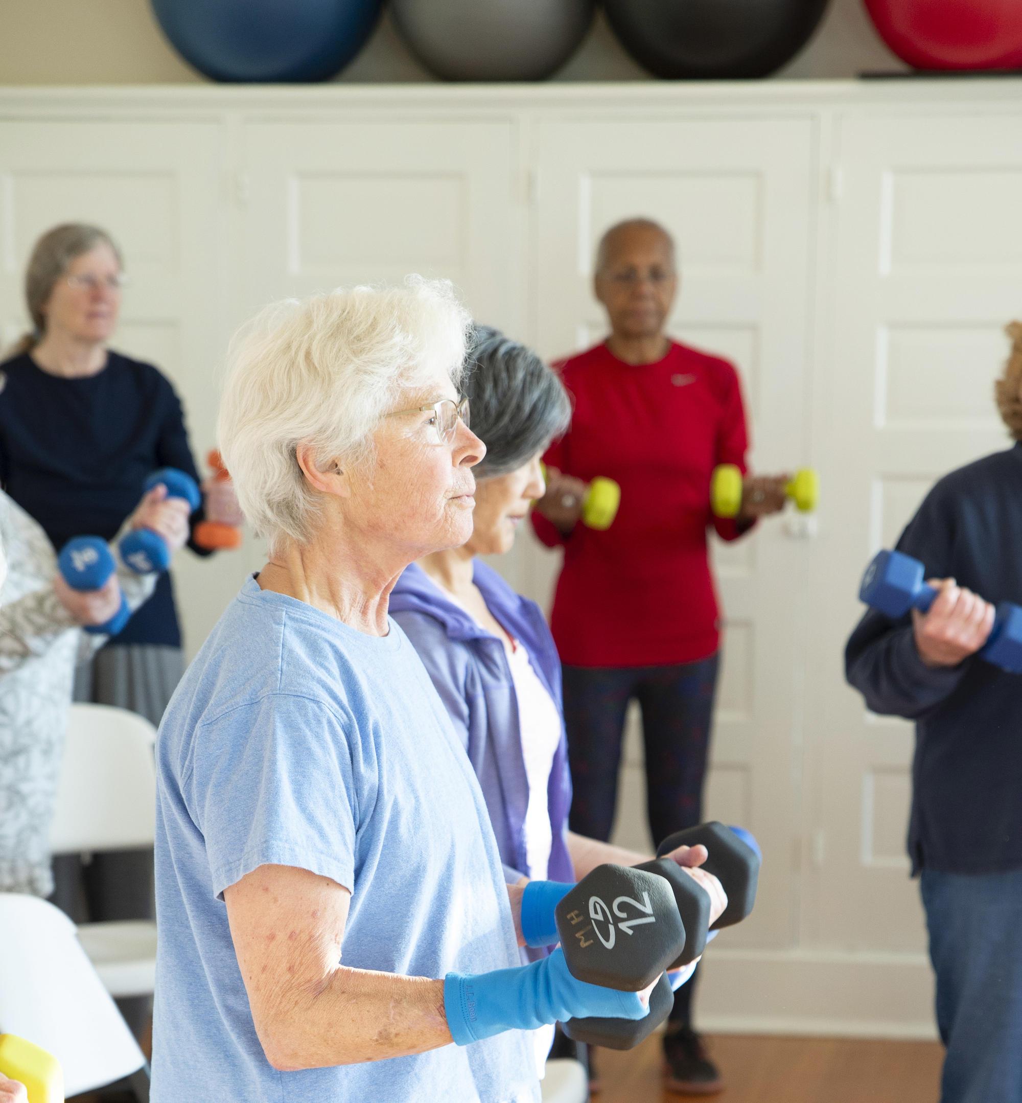 Older women stand in circle lifting hand weights