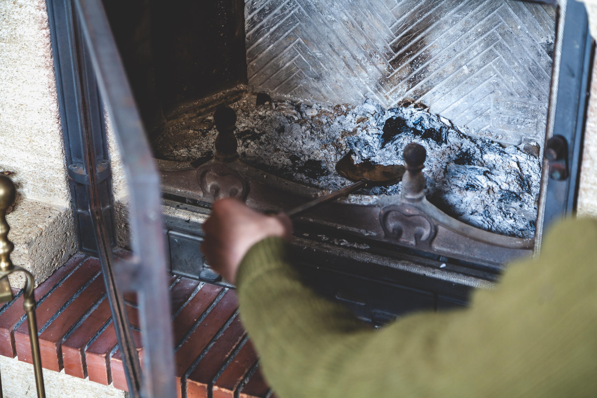 A person poking around ash in a fireplace.