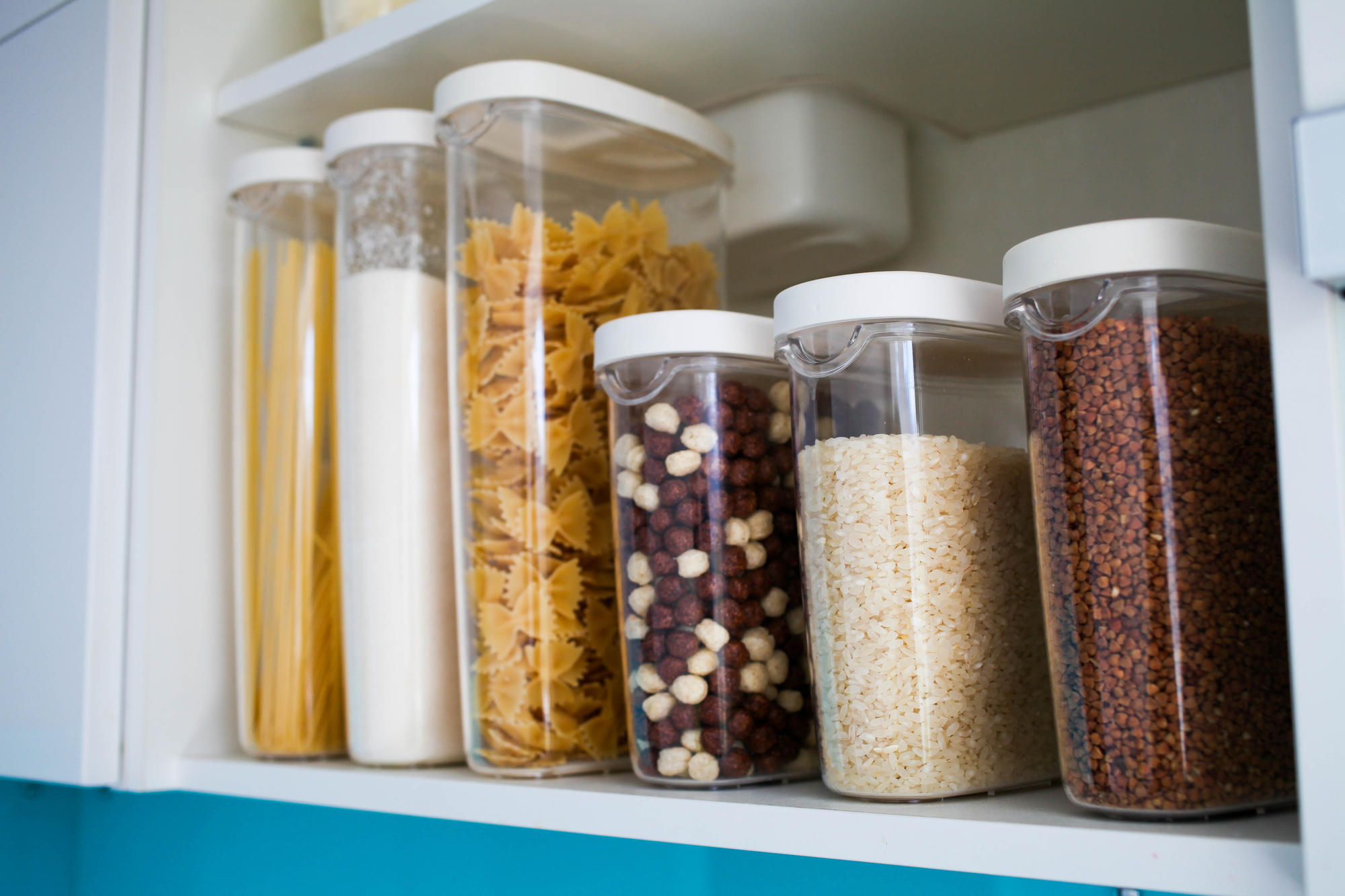 Plastic air-tights containers in a pantry containing rice, pasta, flour, and cereal.