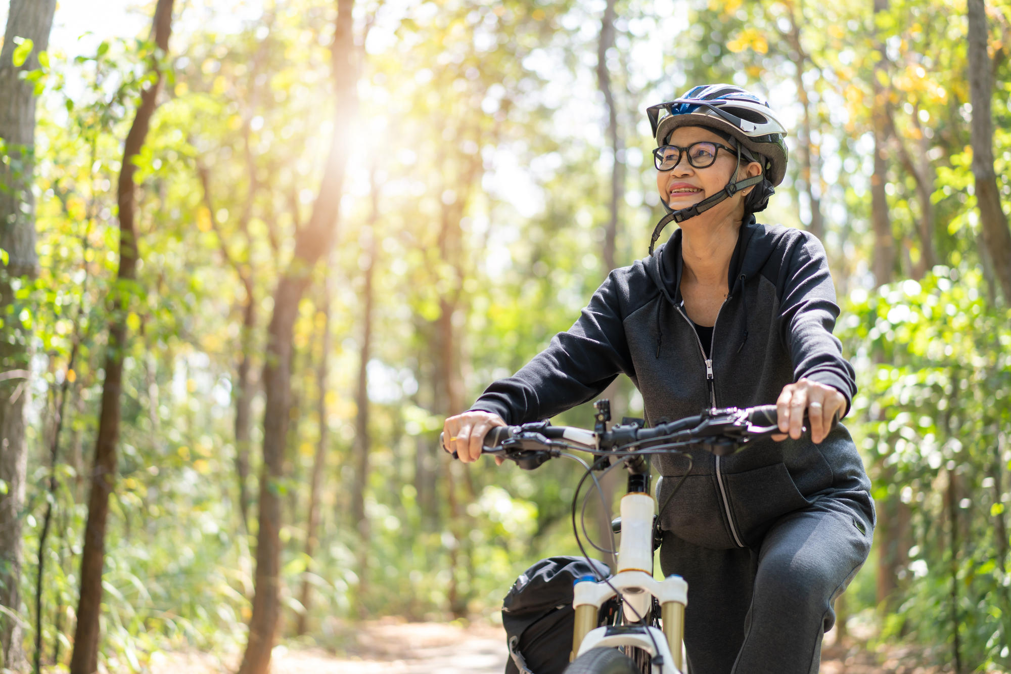 A middle-aged woman biking in a forest.