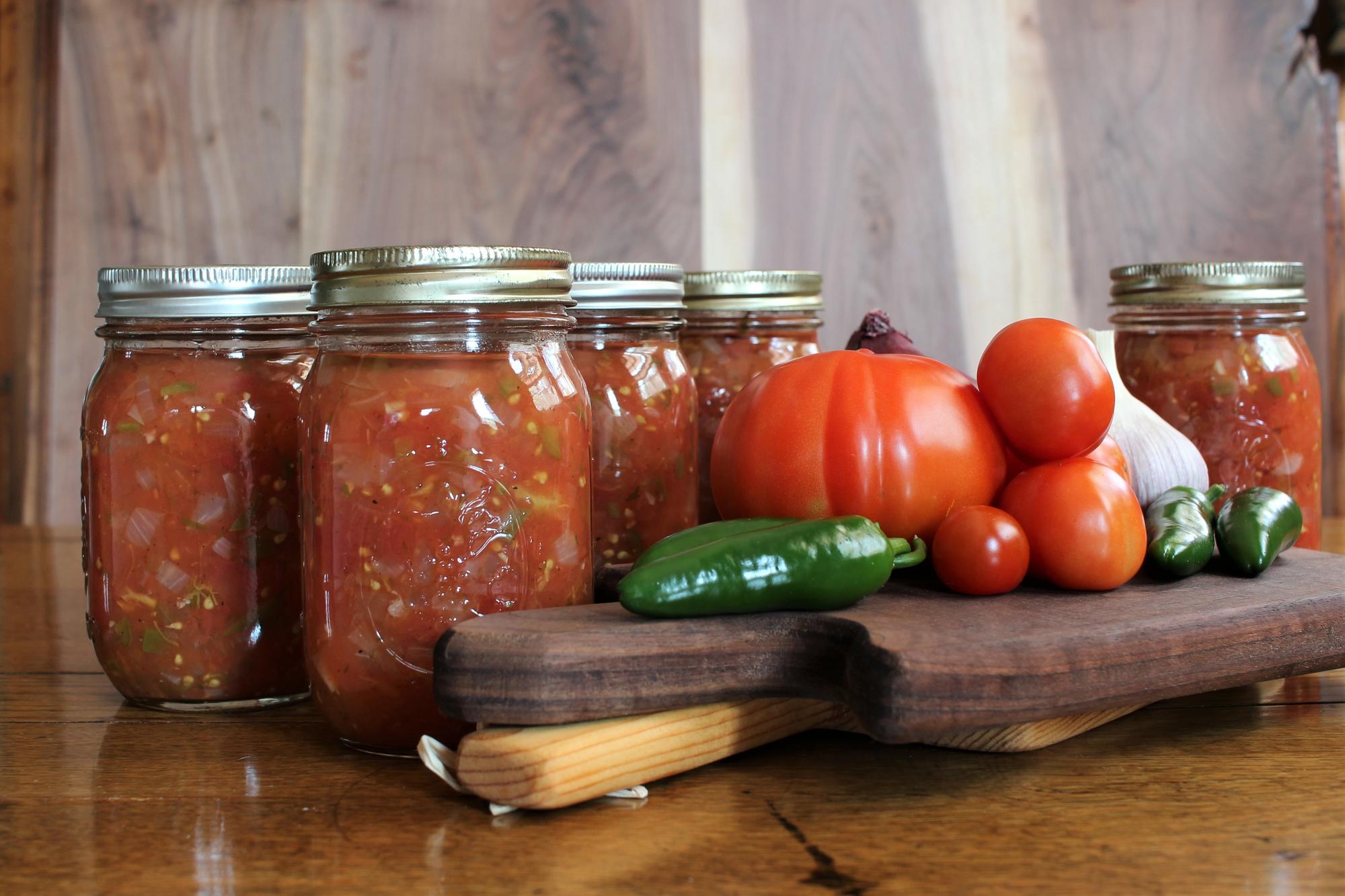 Tomatoes, peppers, and mason jars filled with home made salsa.