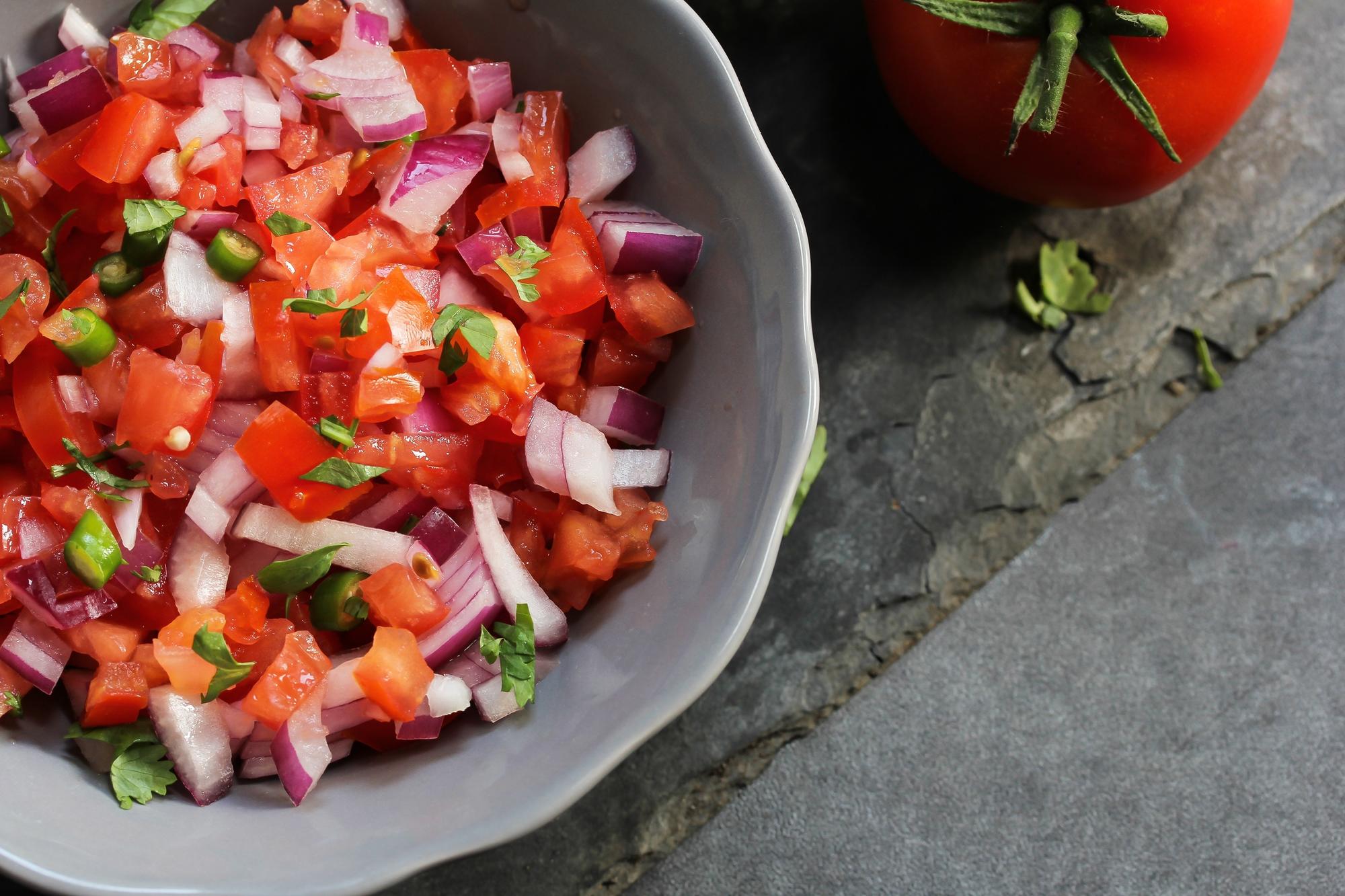 A bowl of fresh salsa and a tomato.