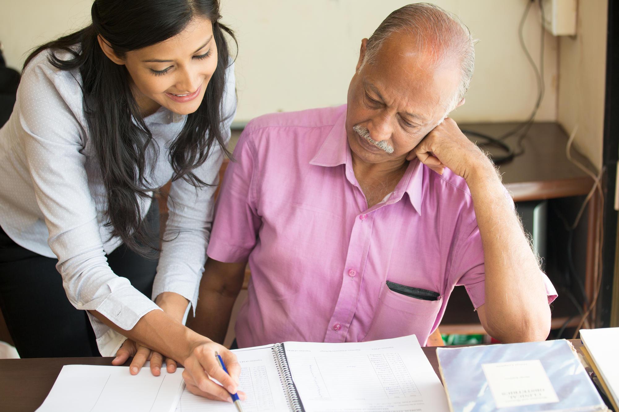 A woman helps and elderly man with paperwork.