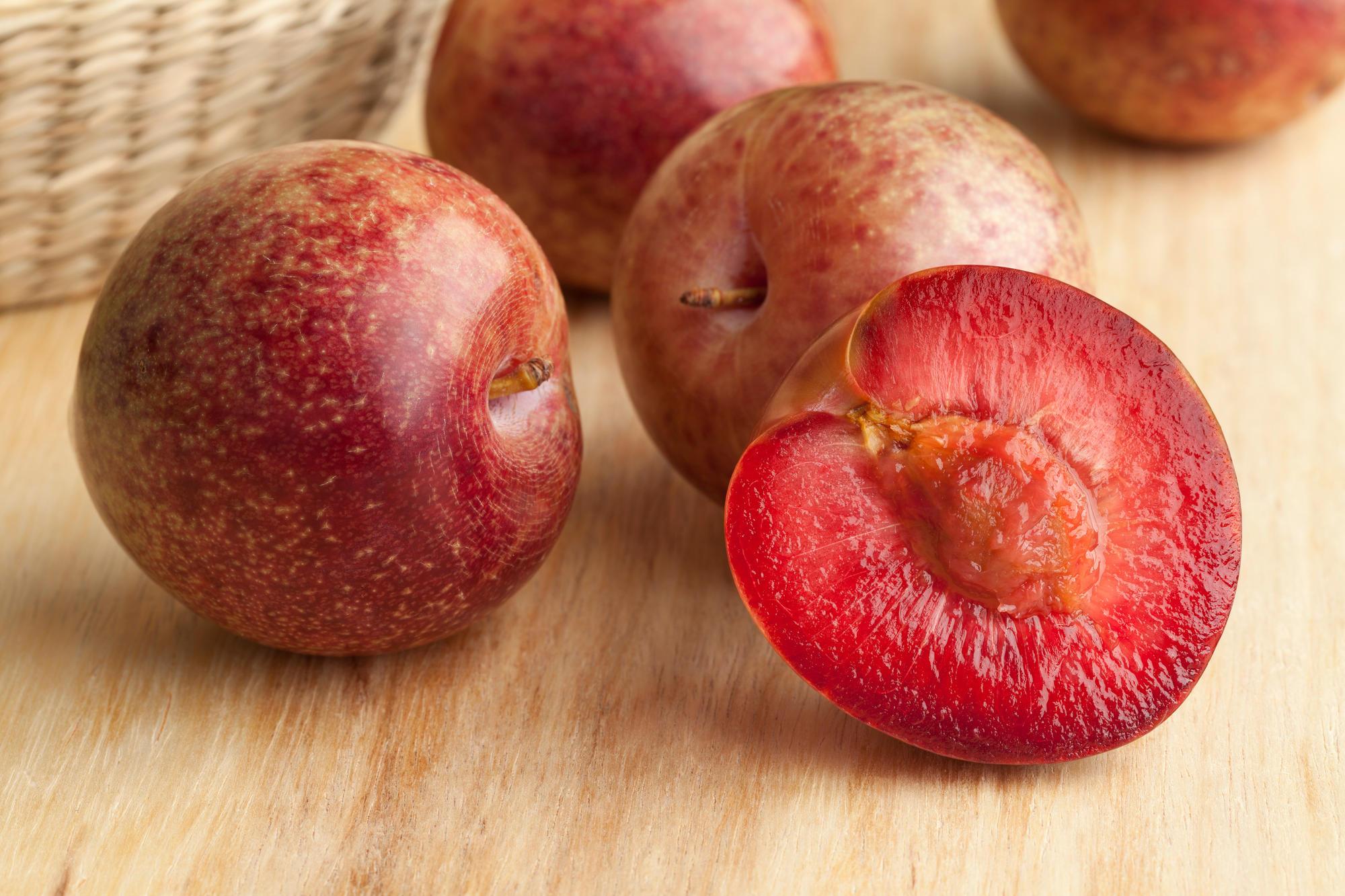 Pluot fruits on a wooden table. One of the fruits is cut in half to display the deep red flesh and the pit.