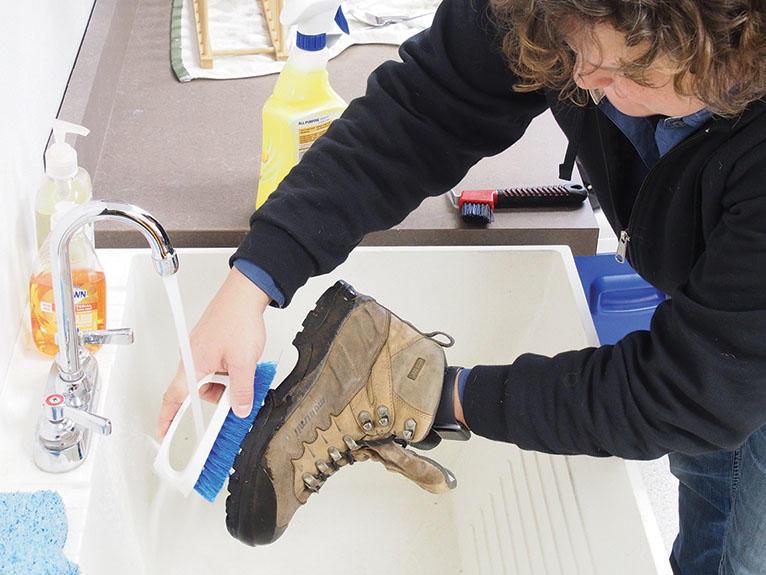 Person washes hiking boot with brush in utility sink