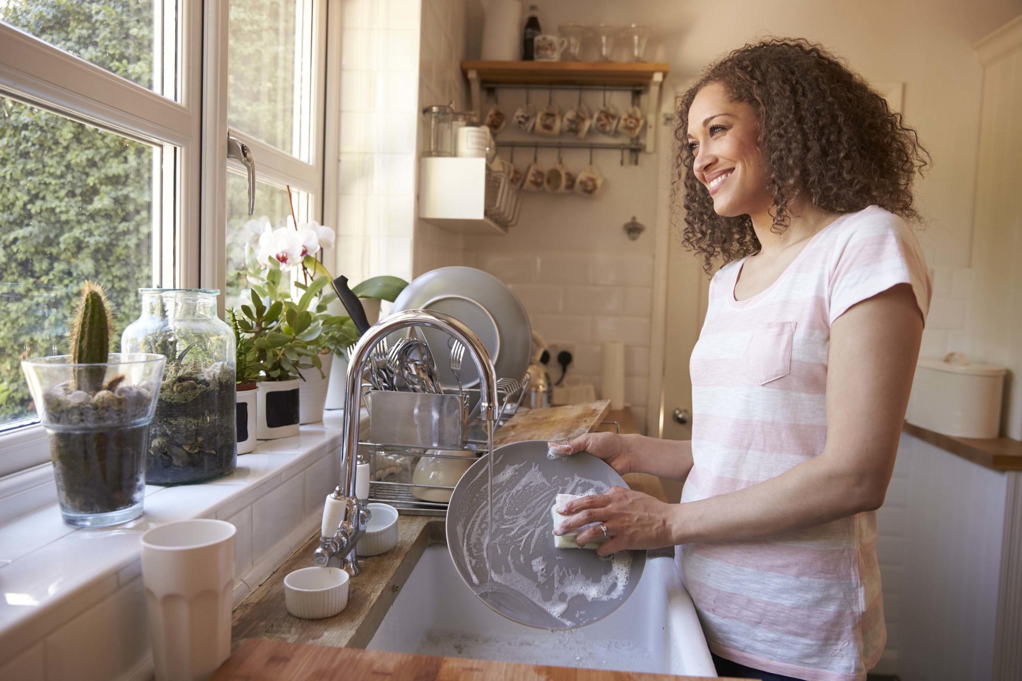 woman washing dishes in kitchen facing window