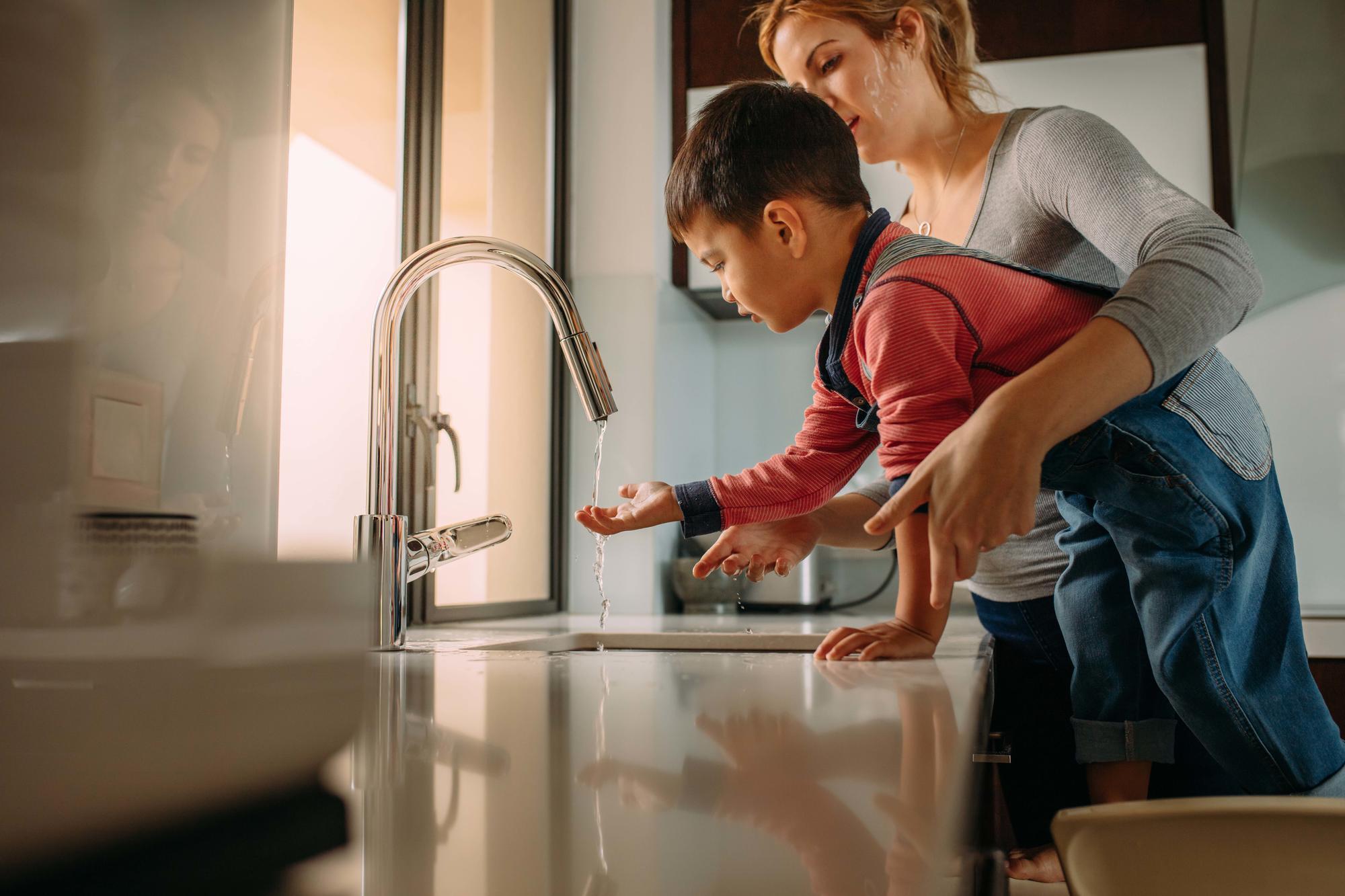 woman helps young boy wash his hands in sink