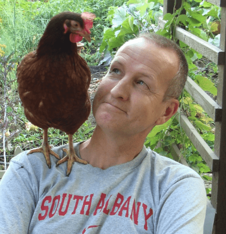 person in garden smiling at chicken on their shoulder