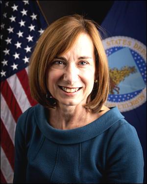 professional profile photo of woman in a blue sweater, with a us flag behind her