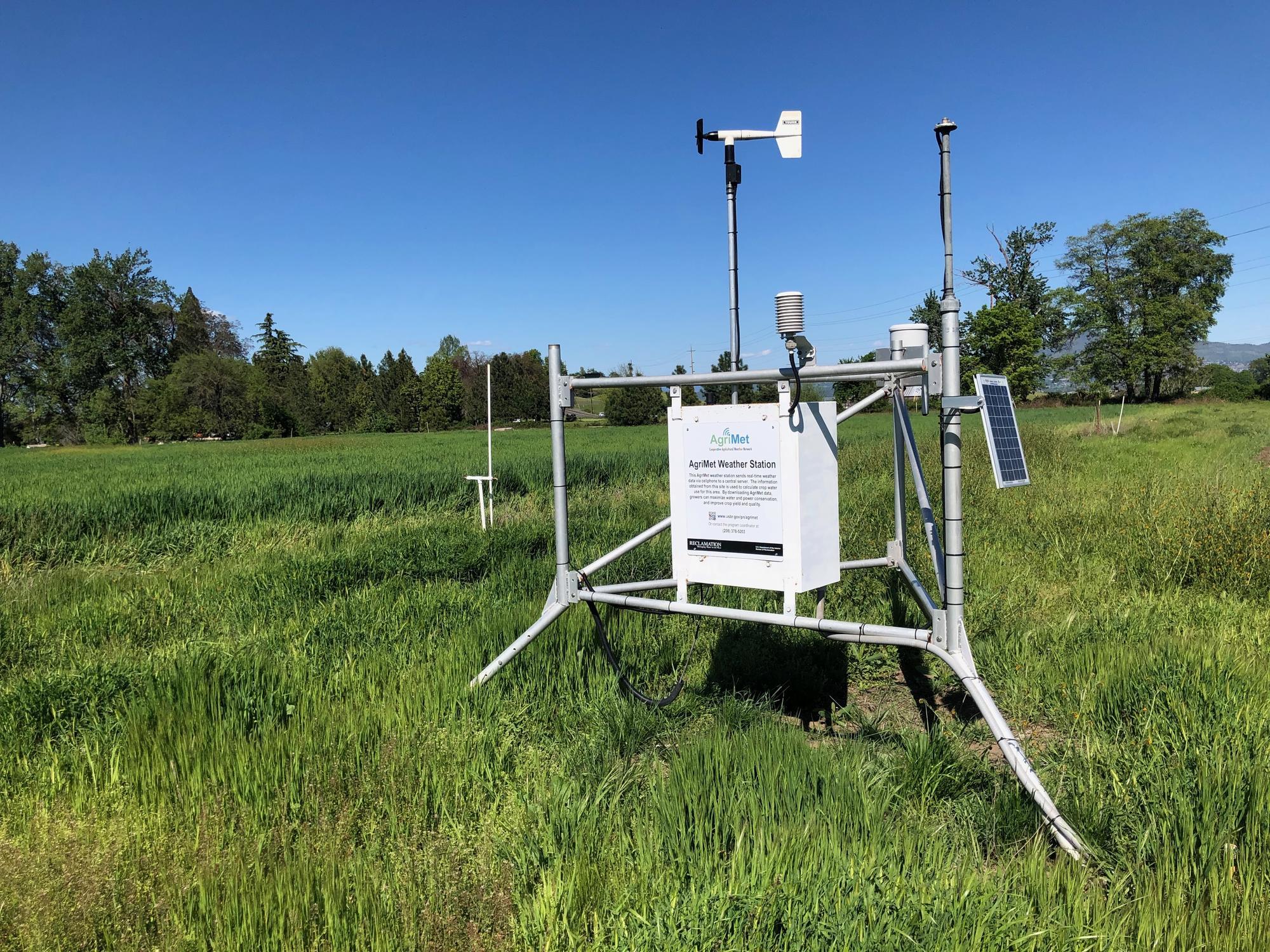 Agrimet weather station in green grass field with blue sky