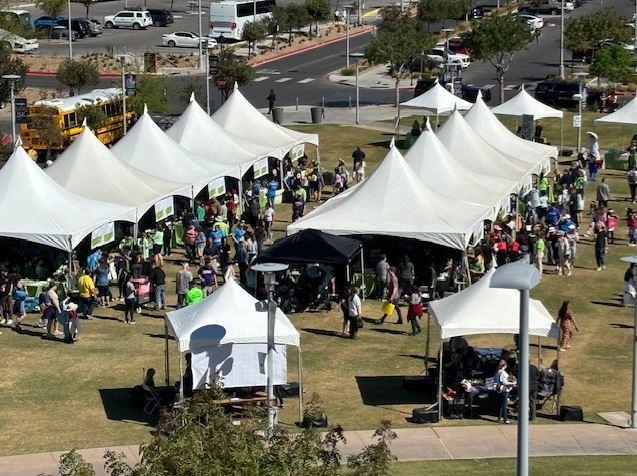 overhead view of a green field with 10 white tents and many people visiting the farmers market