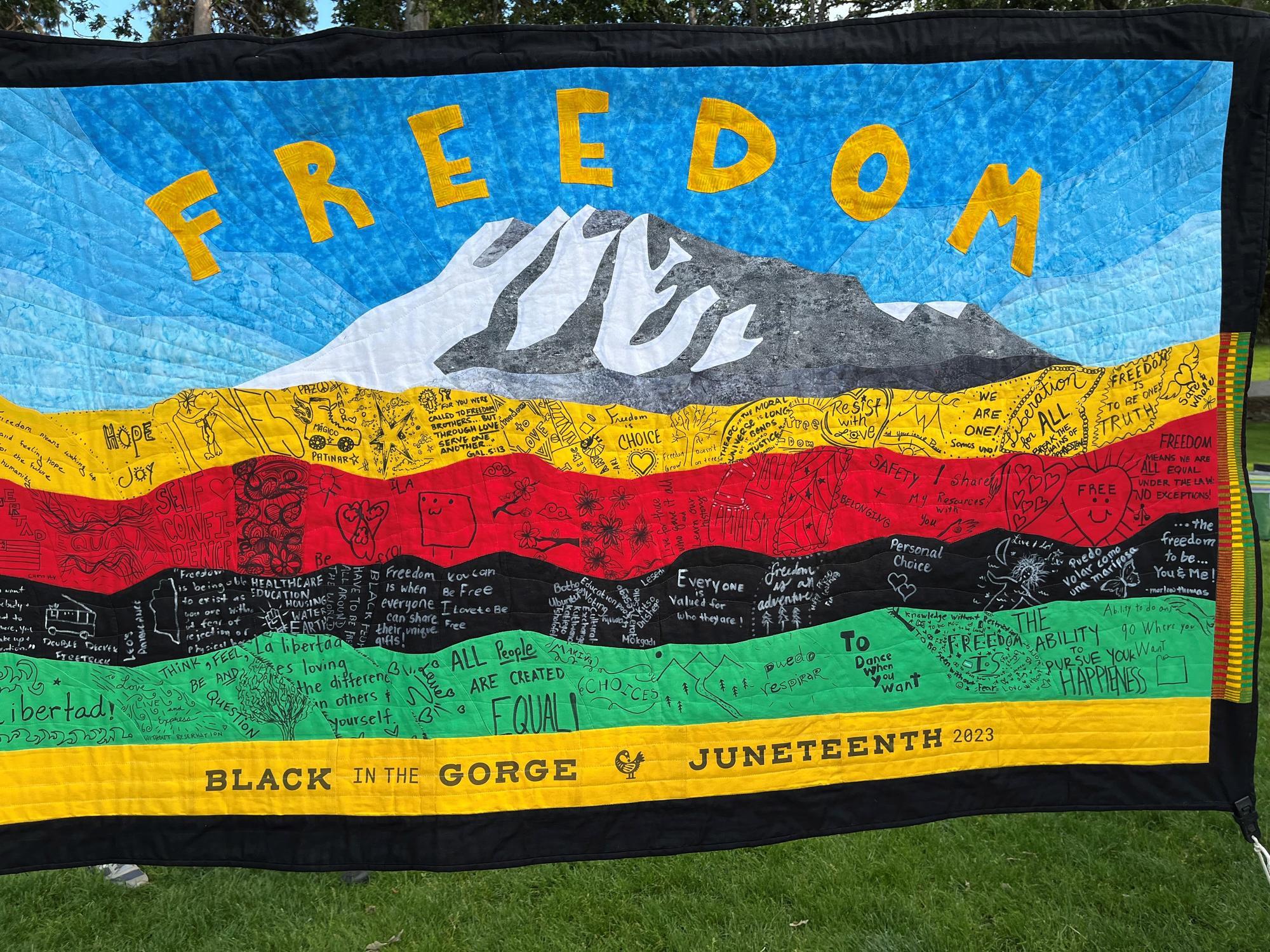 A quilt depicting a mountain, the word freedom, and stripes of yellow, red, black, and green.