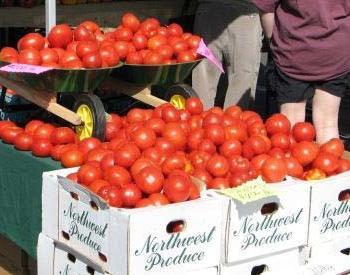 Red tomatoes overflow from stacked produce boxes at a farmer's market.