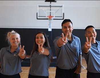 Four youth holding up two fingers on a basketball court