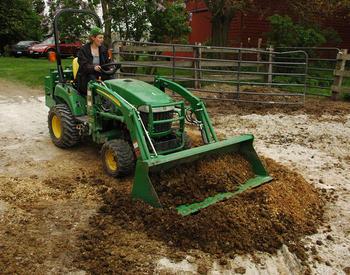 Woman on John Deere tractor scooping from manure pile.