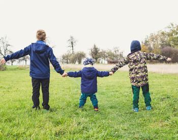 backs of three children holding hands in a field
