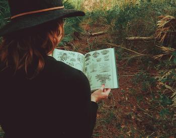 woman reading book of plant drawings outside