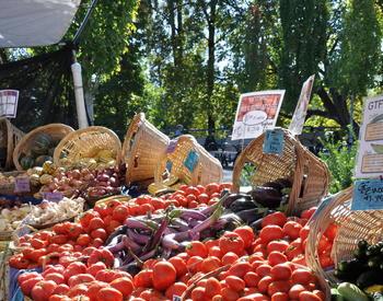 Fresh vegetables are displayed in baskets on a table at a farmers market.
