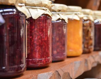 Jars of different kinds of jams are line up on a shelf.