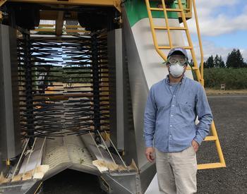 Wei Qiang Yang, associate professor and berry Extension agent for Oregon State University Extension Service, stands in front of a blueberry harvester that uses a soft catch mechanism.