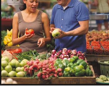 A man and woman look at produce at a farmers market.