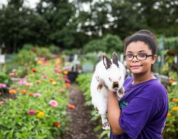 A girl holds a rabbit in a flower garden.