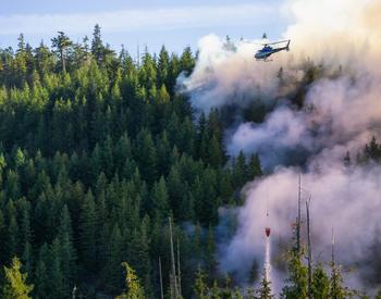 A helicopter flies over a forest fire.