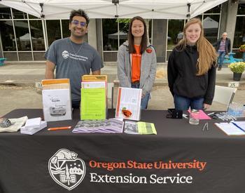A man and two women pose for a photo standing behind a table covered with a black tablecloth that says Oregon State University Extension Service.