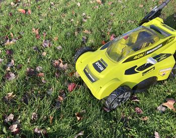 Bright green electric mower being used to mulch fallen leaves and grass into the lawn.