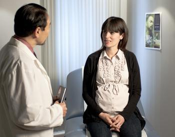 A doctor talks with a pregnant woman in an medical exam room.