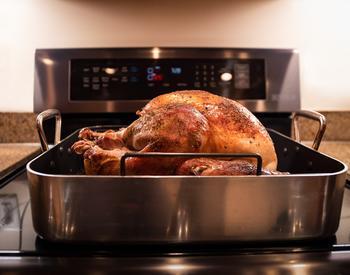 A cooked and seasoned turkey cooling in a roasting pan on a stovetop.